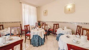 Un comedor con mesas redondas, sillas y una araña.