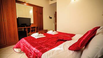 Quarto de hotel com uma cama grande, televisão, guarda-roupa e escrivaninha com cadeira.
