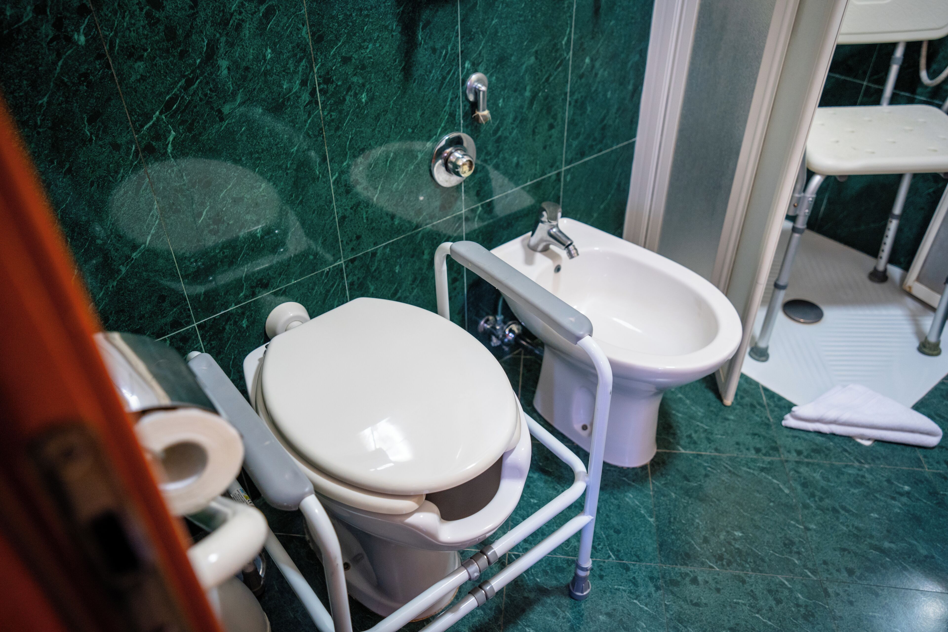 Un baño con inodoro, bidé y un banco accesible para sillas de ruedas.