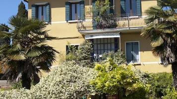 Stunning two-story building surrounded by lush greenery and palm trees, featuring a balcony with a metal railing.