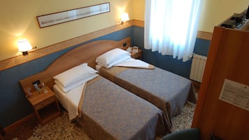 Habitació d'hotel amb dos llits individuals, una tauleta de nit de fusta, un escriptori i una cadira.