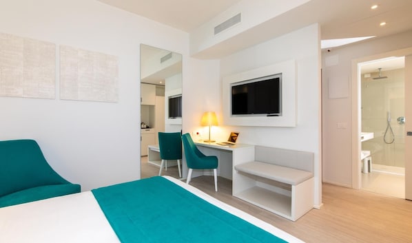Quarto de hotel moderno com cama, escrivaninha com cadeira, televisão e chuveiro.