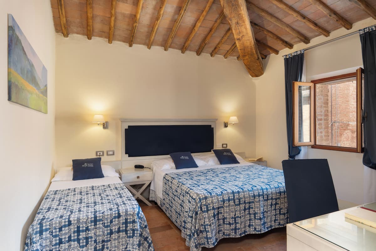 A bedroom with two beds, a wooden ceiling, a desk, and a window with curtains.