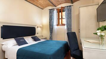 Habitación de hotel con cama, escritorio, silla, televisión y ventana con cortinas.