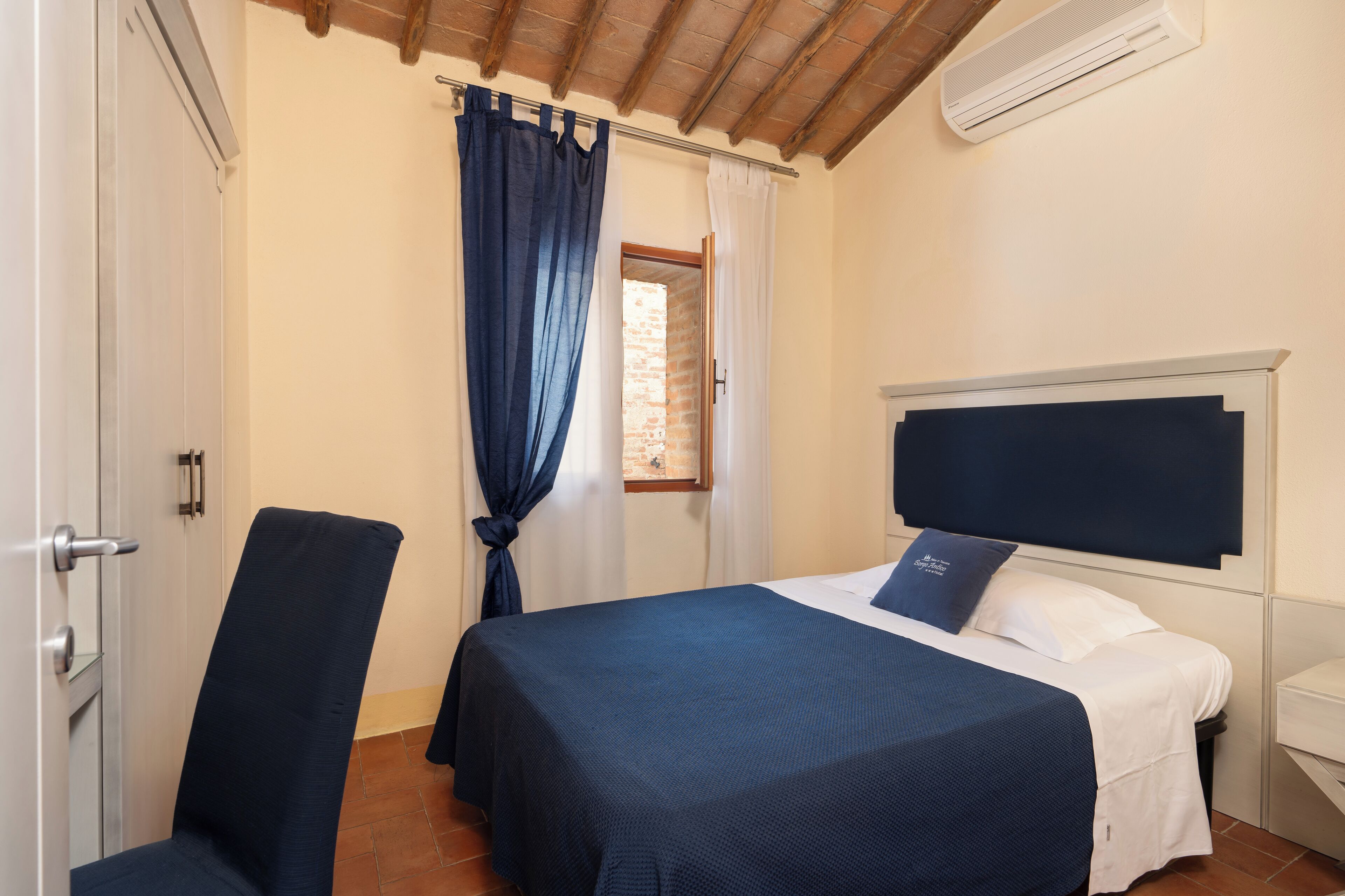 Una camera da letto con un letto, una sedia, un comodino e una finestra con tende.