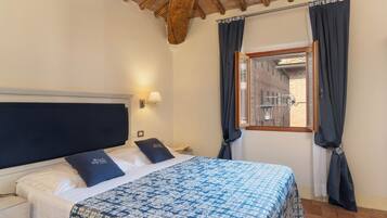 Un dormitorio con cama, mesita de noche, lámpara, ventana con cortinas y vista a un edificio.