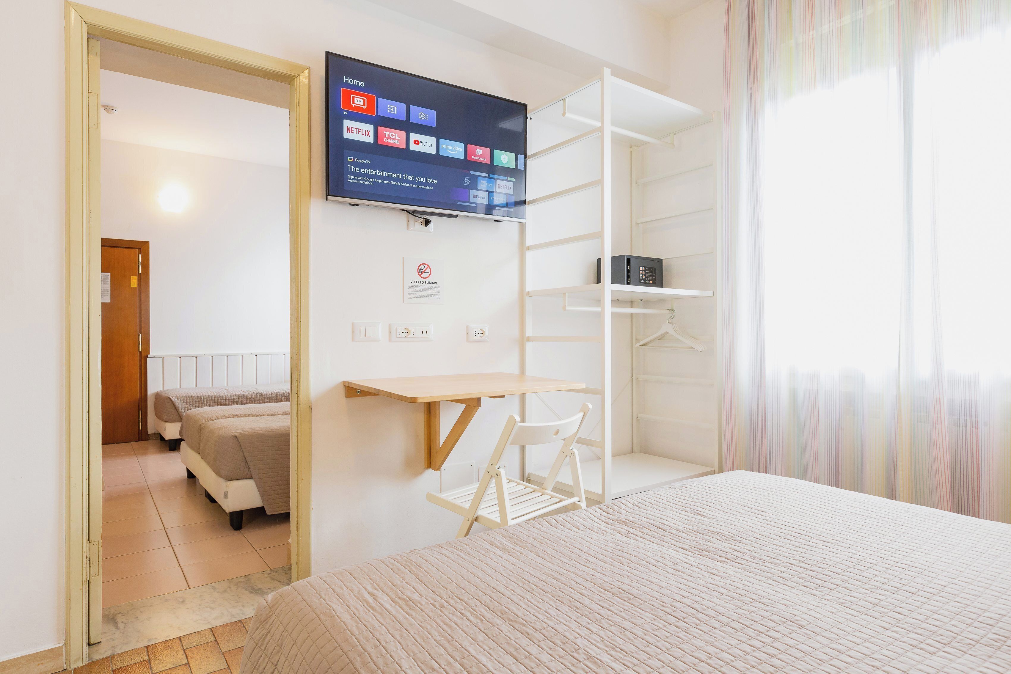 Habitación de hotel con cama, escritorio, silla, televisor montado en la pared y vista a otra habitación.