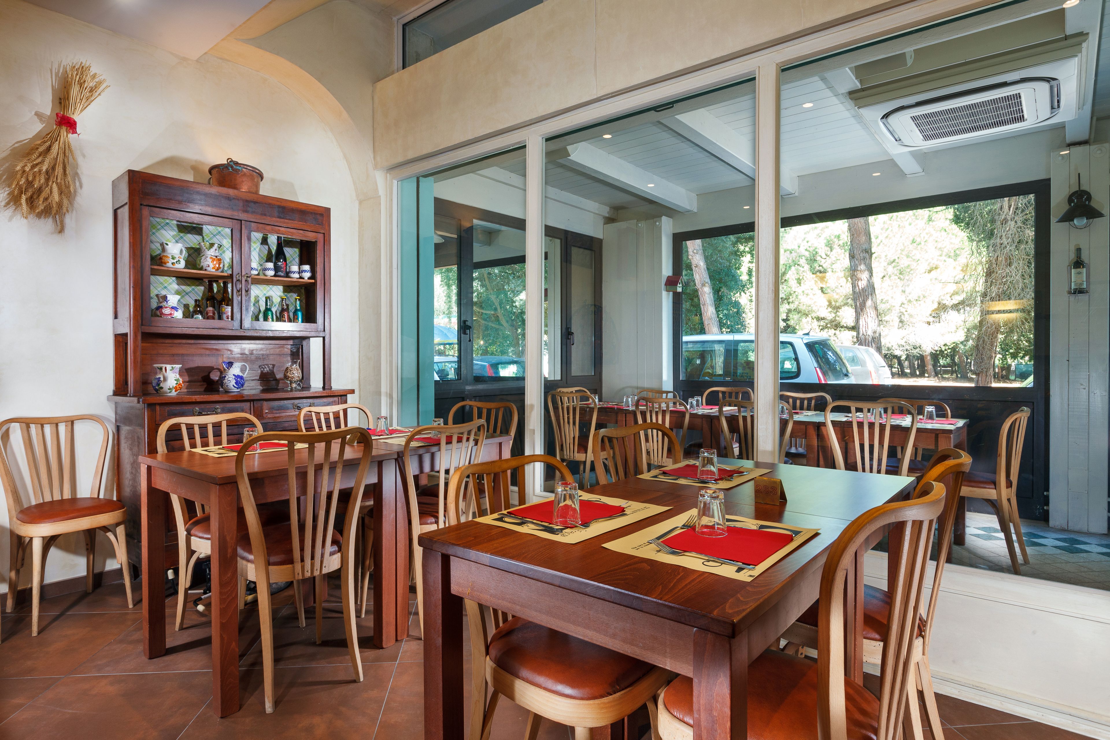 Un comedor con mesas y sillas de madera, un aparador tipo buffet y amplias ventanas con vistas al exterior.