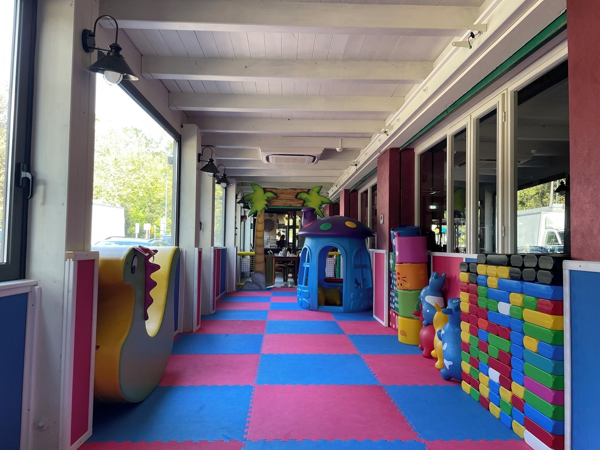 A children's play area with colorful mats, play structures, and a view of the street.