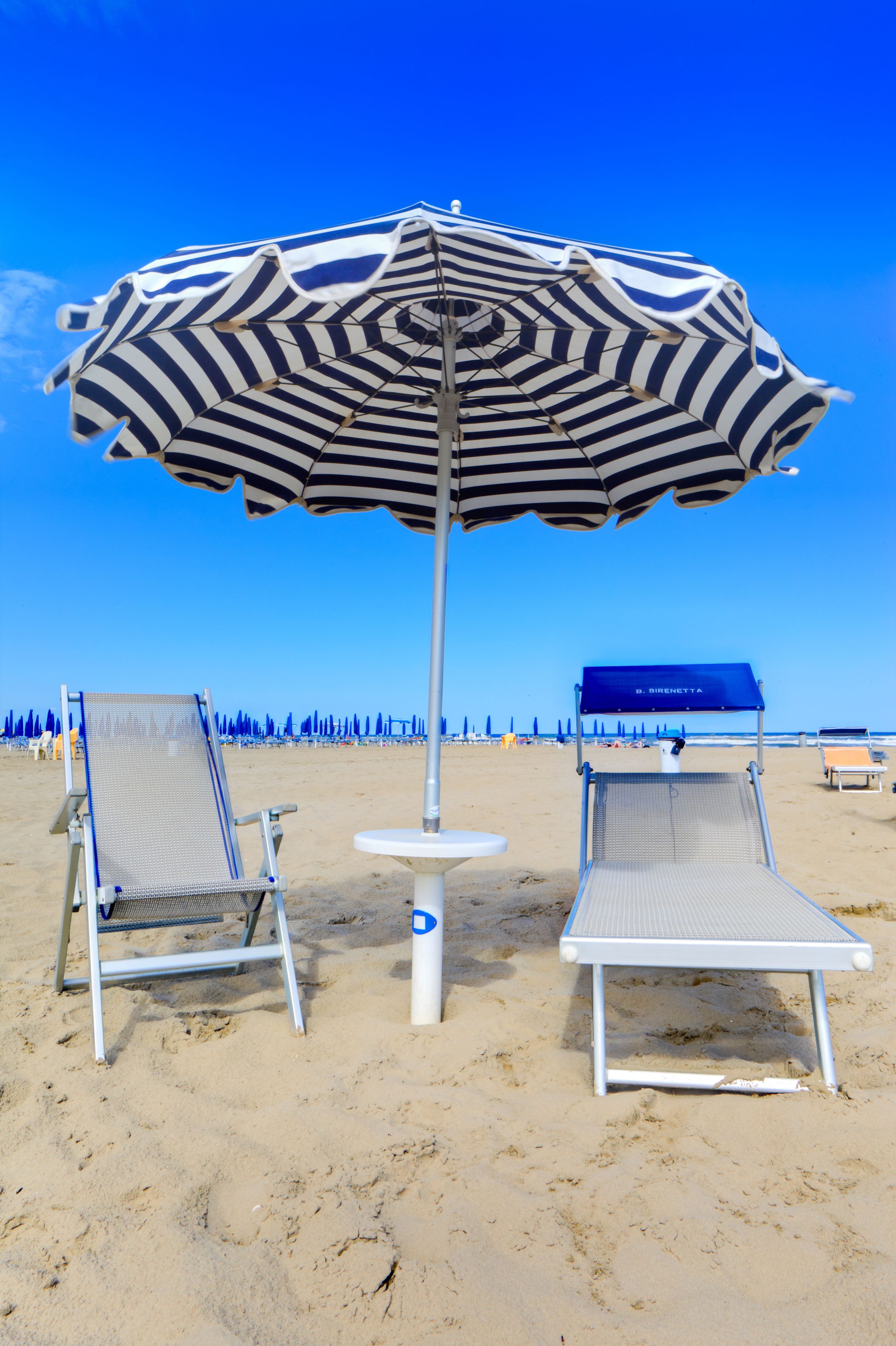 A beach with two lounge chairs and a striped umbrella.