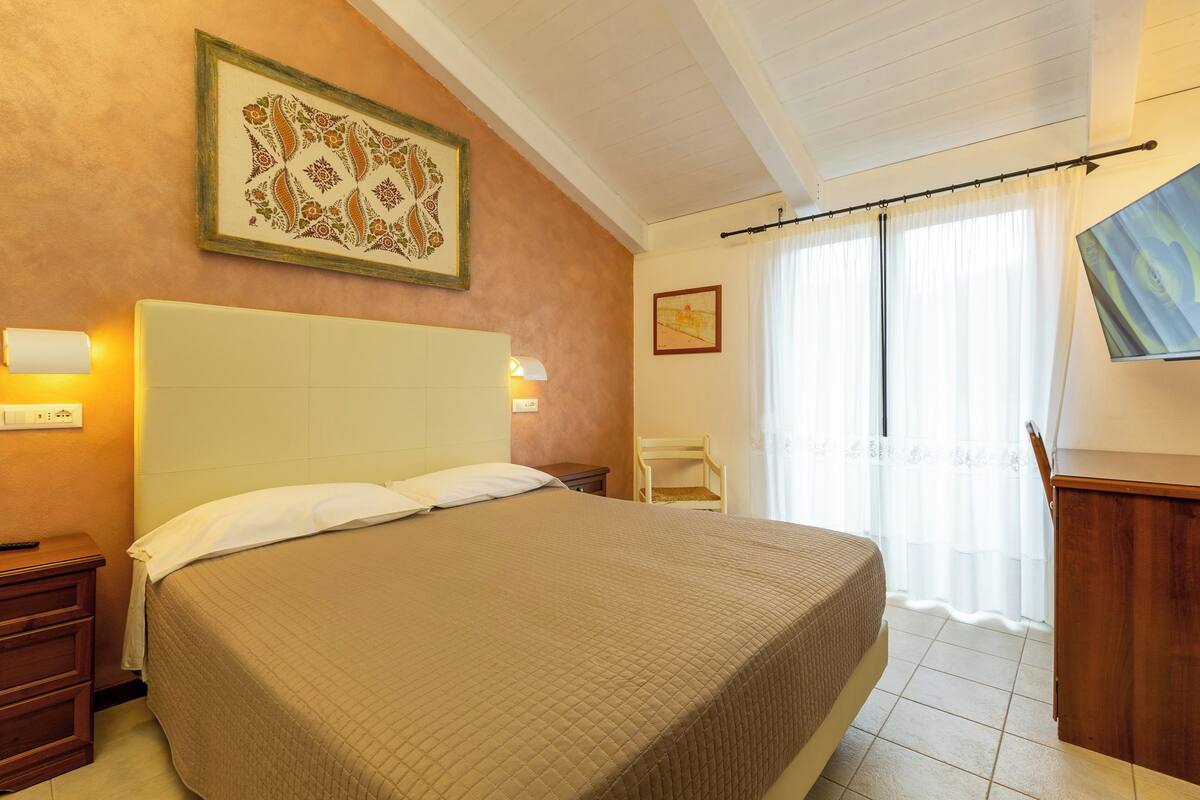 A hotel room with a large bed, a nightstand, a chair, and a desk.