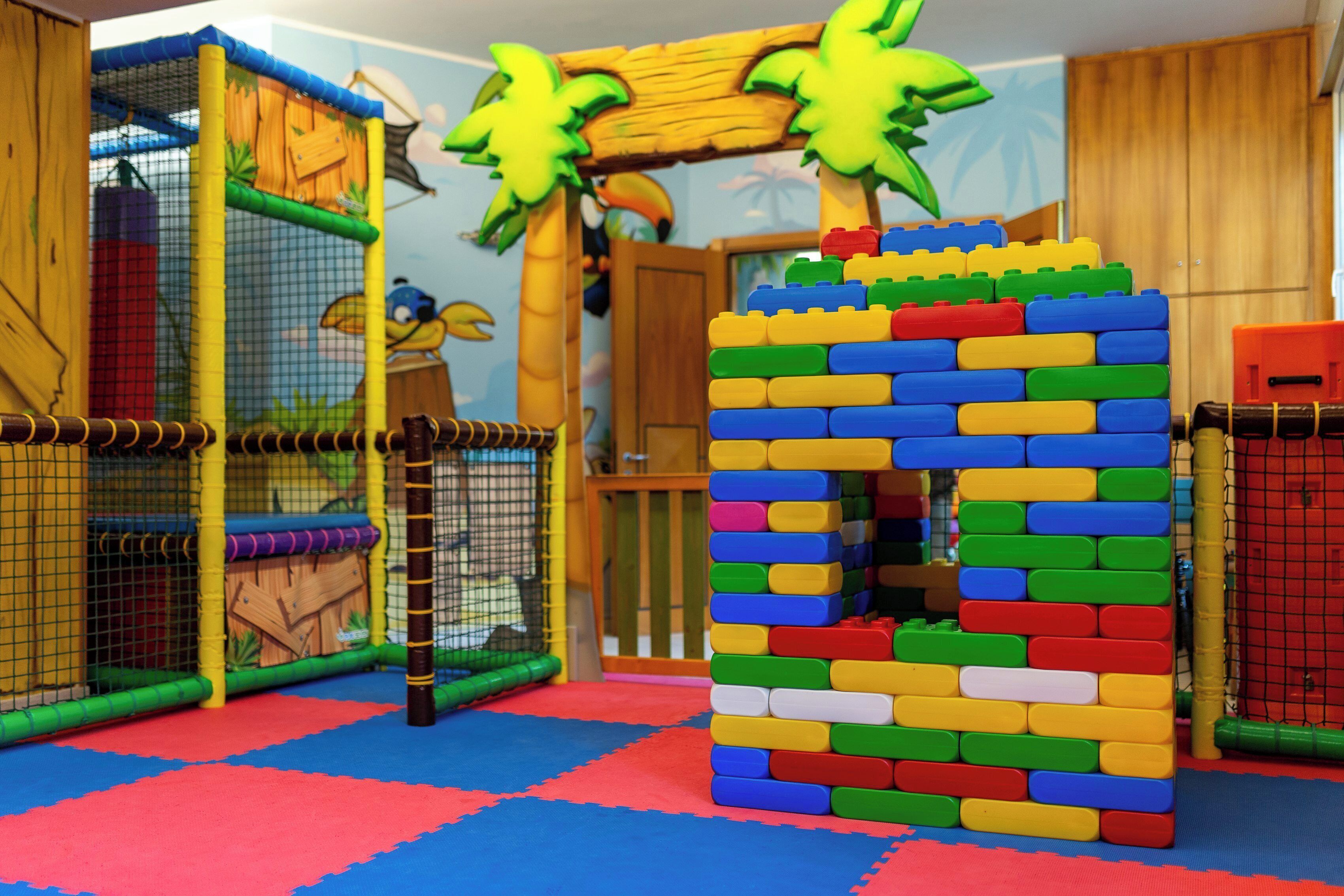 Ein Spielbereich mit einer bunten Spielkonstruktion, einem Netzbereich und einem hölzernen Spielhäuschen.