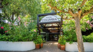A hotel entrance with a sign reading "Hotel Columbia," surrounded by lush greenery and flowering plants. - Columbia (Ravenna)