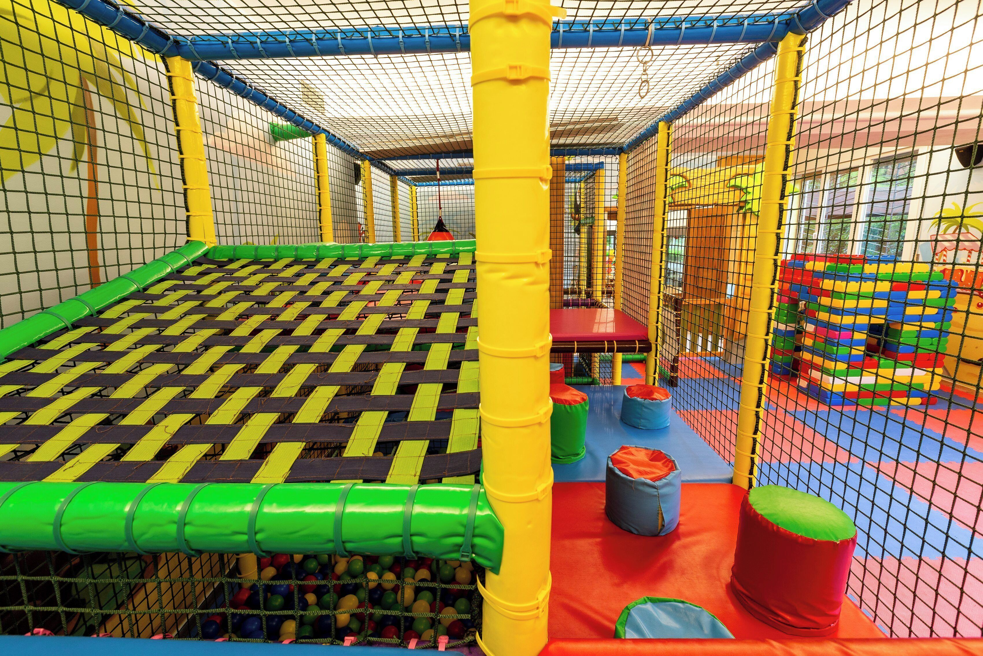 Un espace de jeux doté d’un sol en filet, d’éléments de jeu colorés et d’obstacles rembourrés.