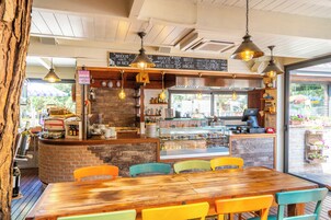 Interior de un restaurante con una mesa de madera y sillas coloridas, una barra con una máquina de café y un menú en una pizarra.