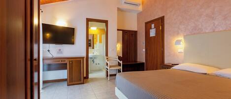 A hotel room with a bed, a desk, a chair, a television, and a bathroom visible through an open door.