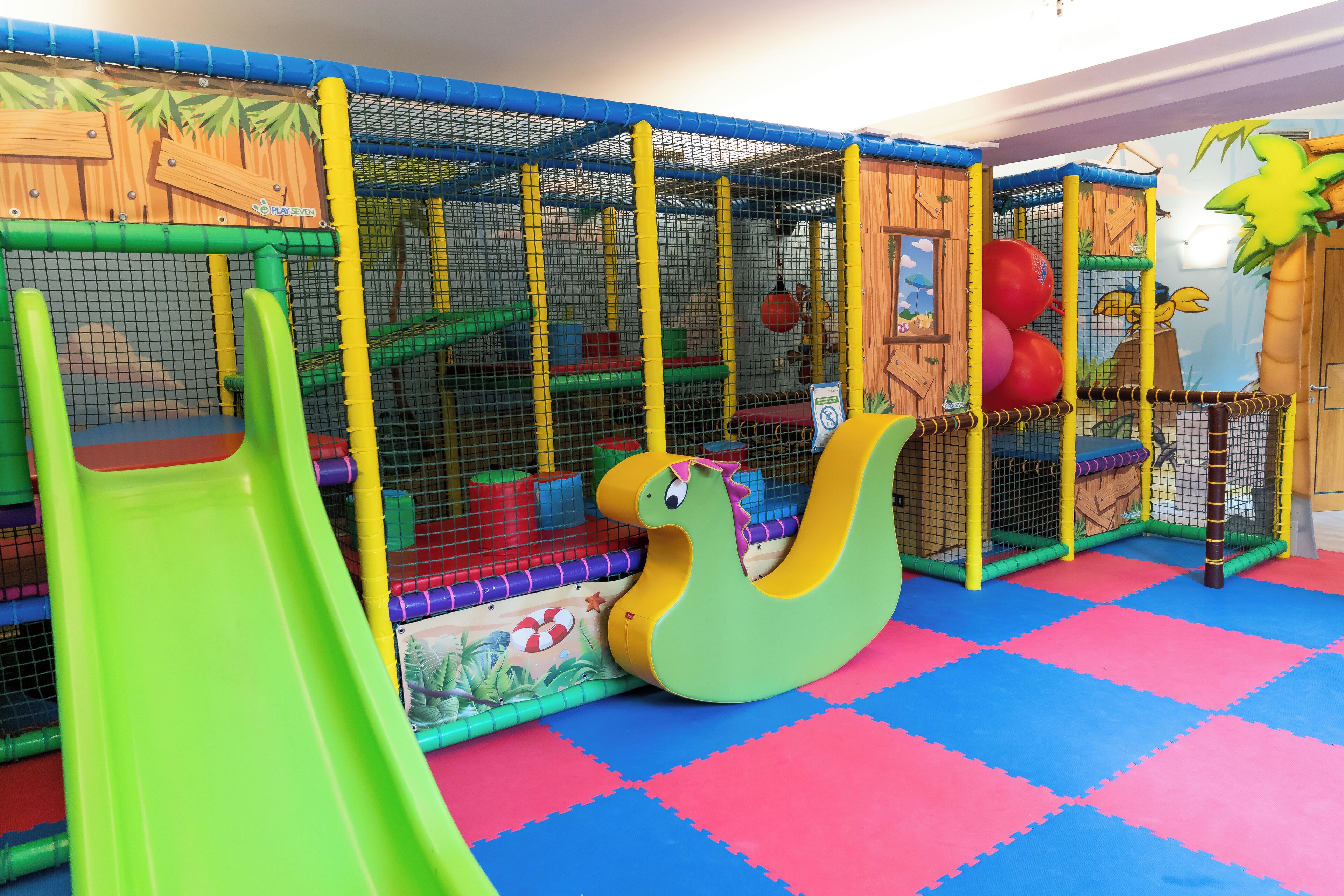Espaço de recreação infantil com escorrega, rede de escalada e um grande brinquedo de cobra verde.
