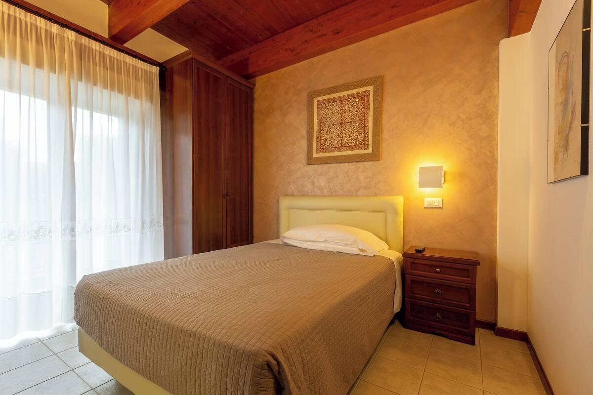 A bedroom with a bed, a nightstand, a wall-mounted light, and a decorative wall piece.