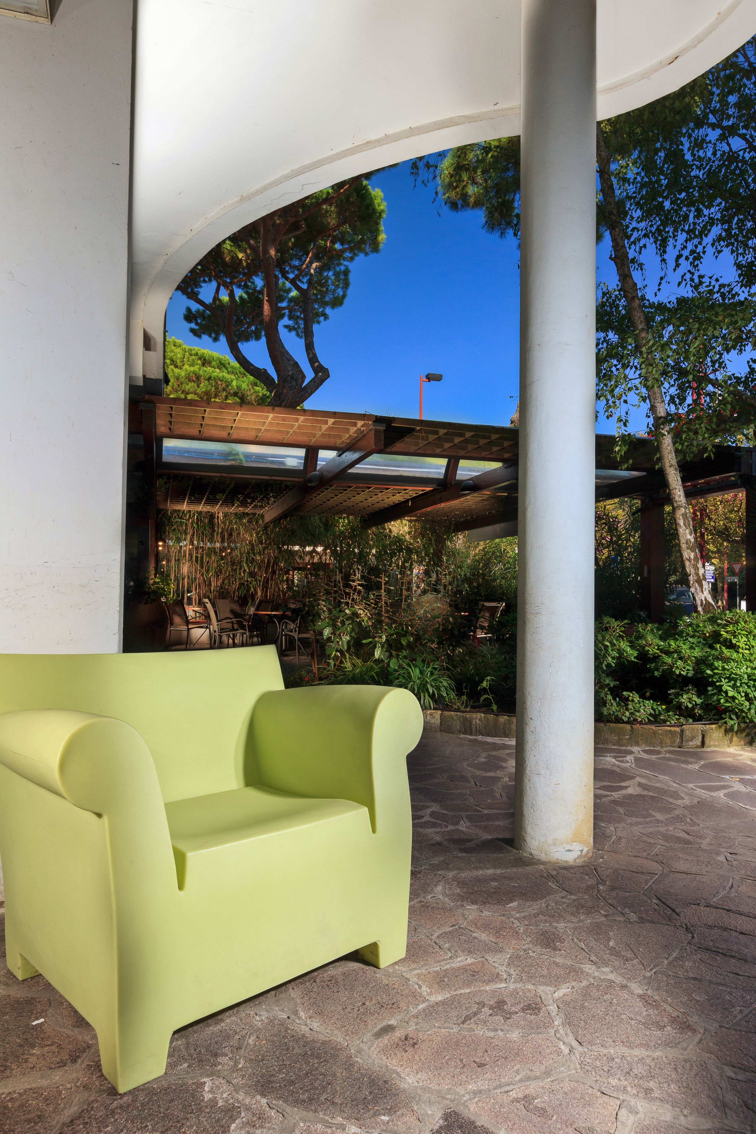 A covered outdoor seating area with a light green sofa, stone flooring, and a pergola structure.