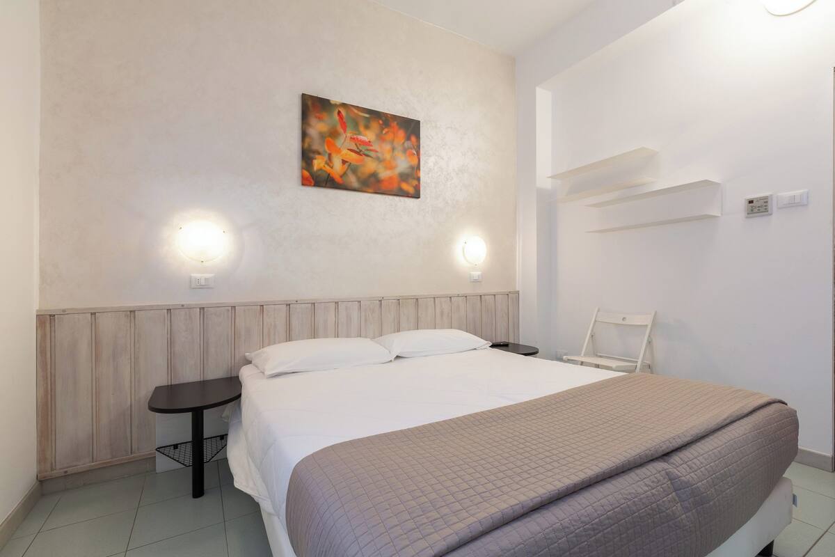 A neatly arranged hotel room with a bed, bedside table, and a wall-mounted light fixture.