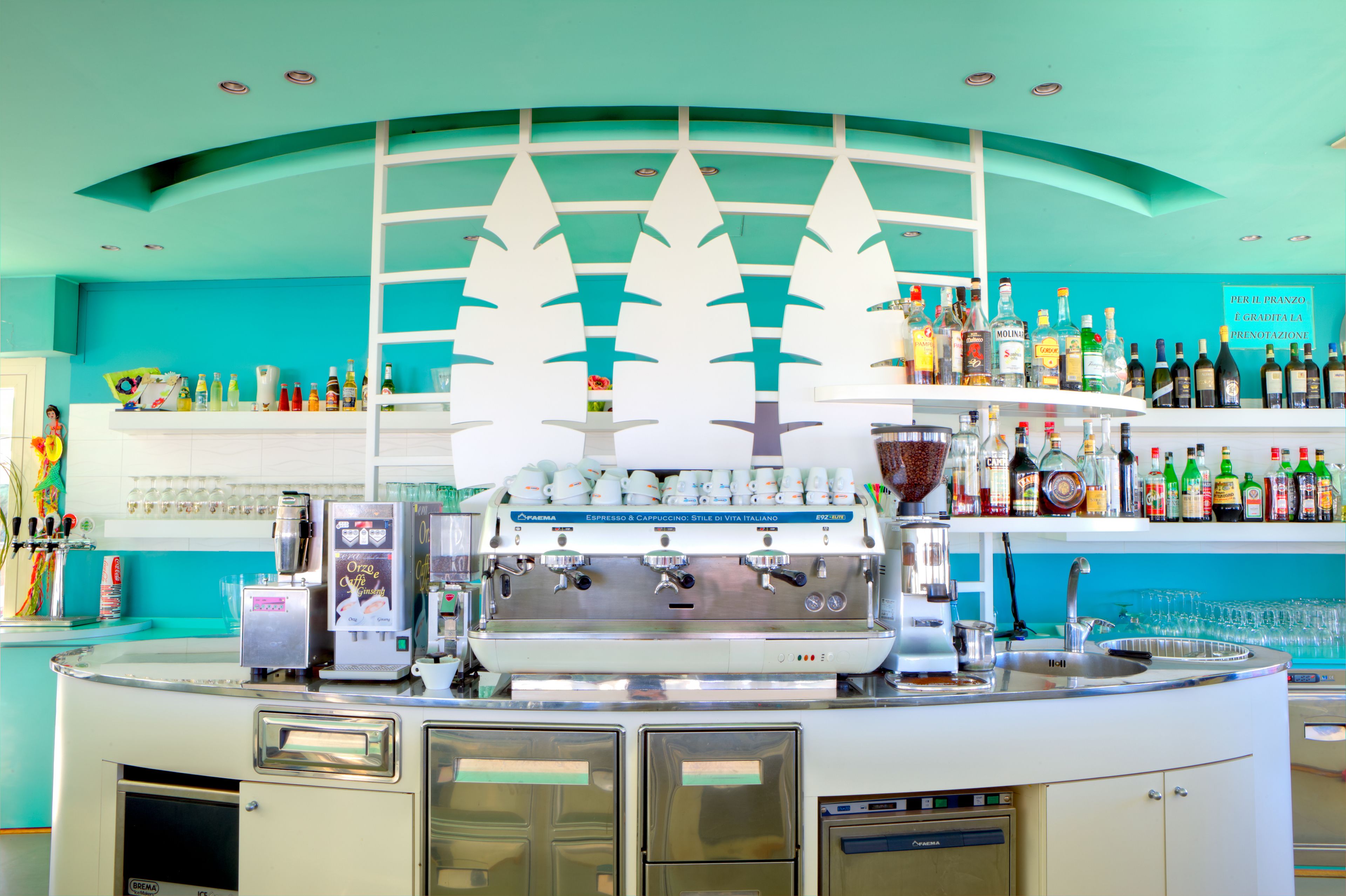 A bar area with a coffee machine, shelves with bottles, and a teal-colored ceiling.