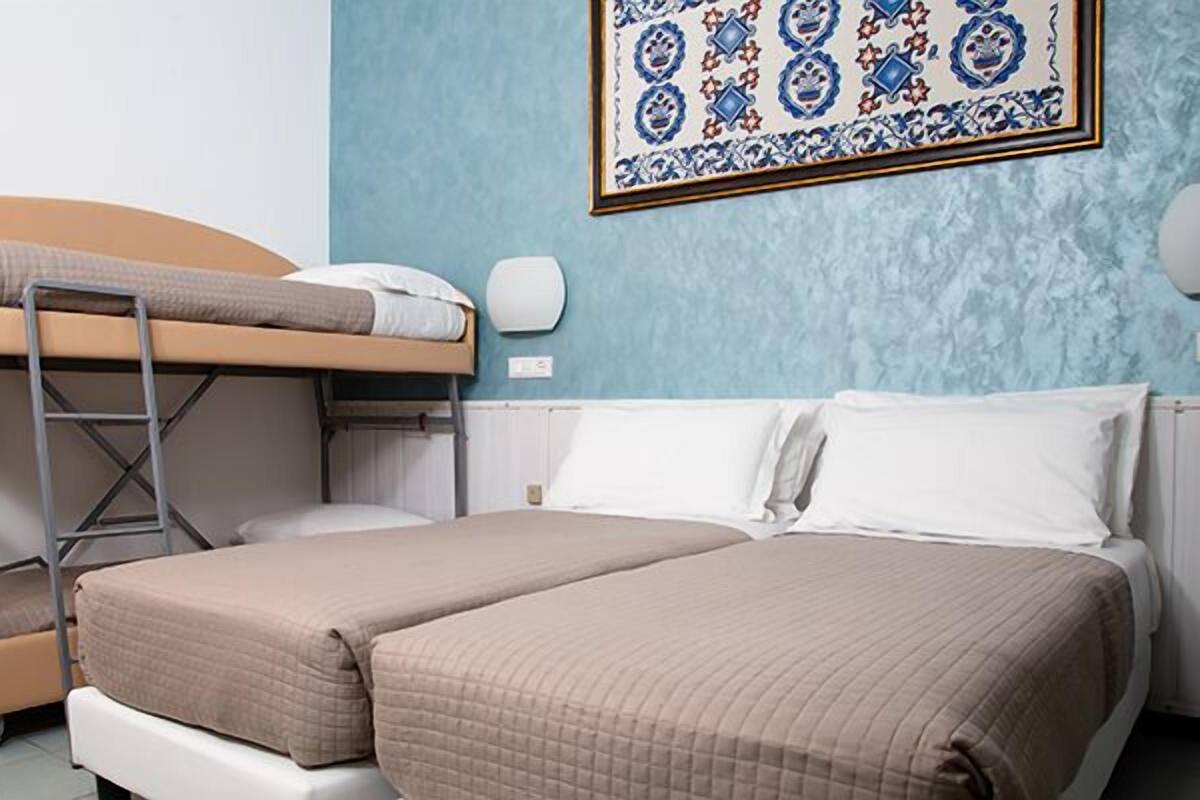 A room with a bunk bed, a lower bed, and a wall-mounted light fixture.