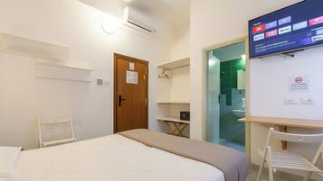A hotel room with a bed, a desk, a chair, a TV mounted on the wall, and a door.