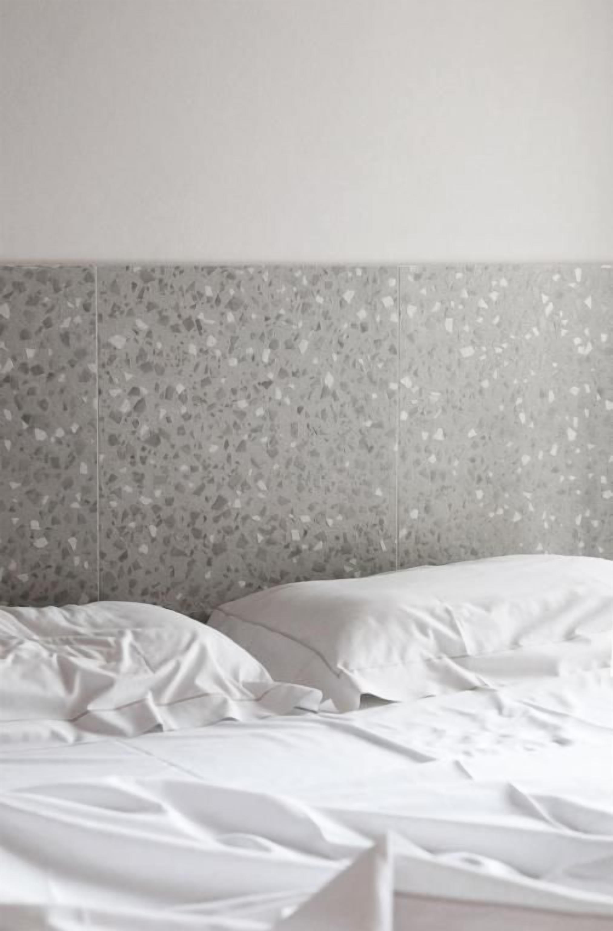 A bed with white bedding, a headboard with a speckled pattern, and a plain wall.