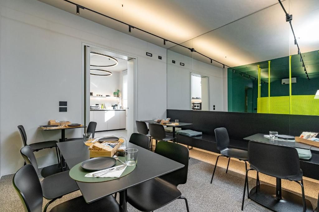 Un espace repas moderne avec des tables et des chaises, une cuisine en arrière-plan et un grand miroir qui reflète l’ensemble de la pièce.