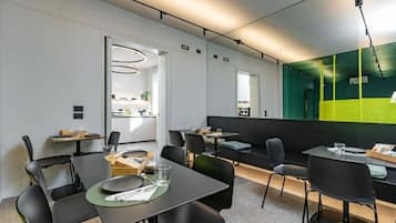 Un espace repas moderne avec des tables et des chaises, une cuisine en arrière-plan et un grand miroir qui reflète l’ensemble de la pièce.