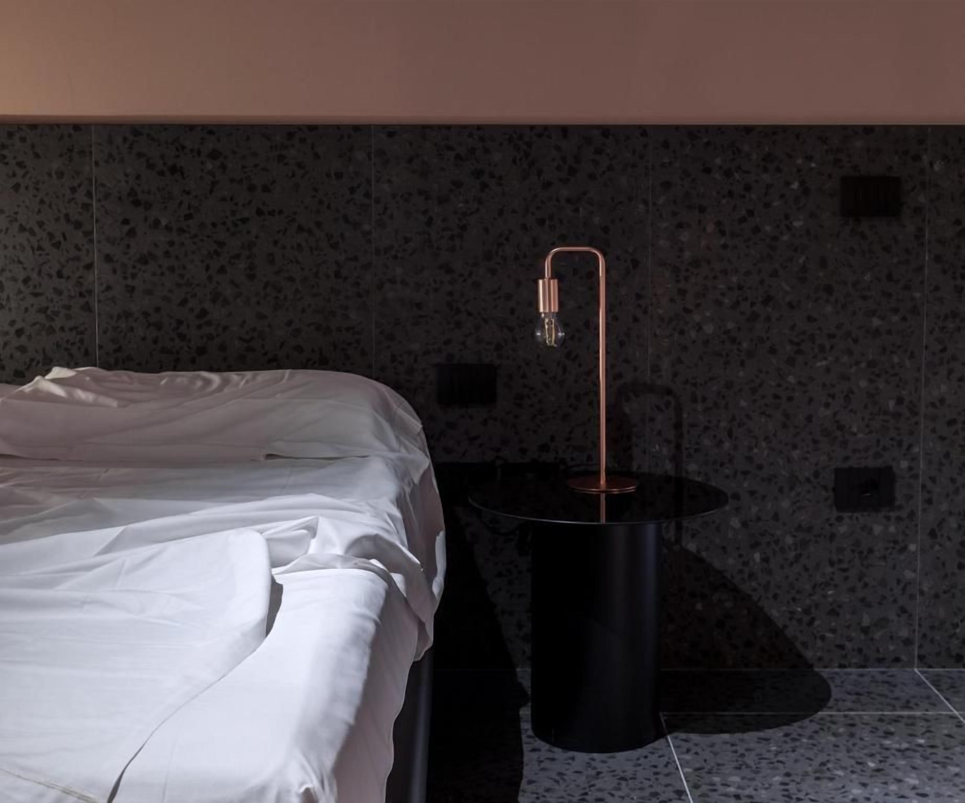 Una habitación de hotel con una cama, una mesita redonda negra y una lámpara moderna.