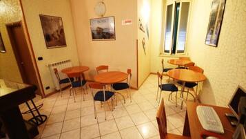 A room with a tiled floor, multiple round tables with chairs, a desk with a computer, and a window with blinds.