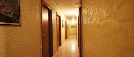 Un couloir étroit, doté d’un sol carrelé et de portes en bois, qui mène à plusieurs pièces.