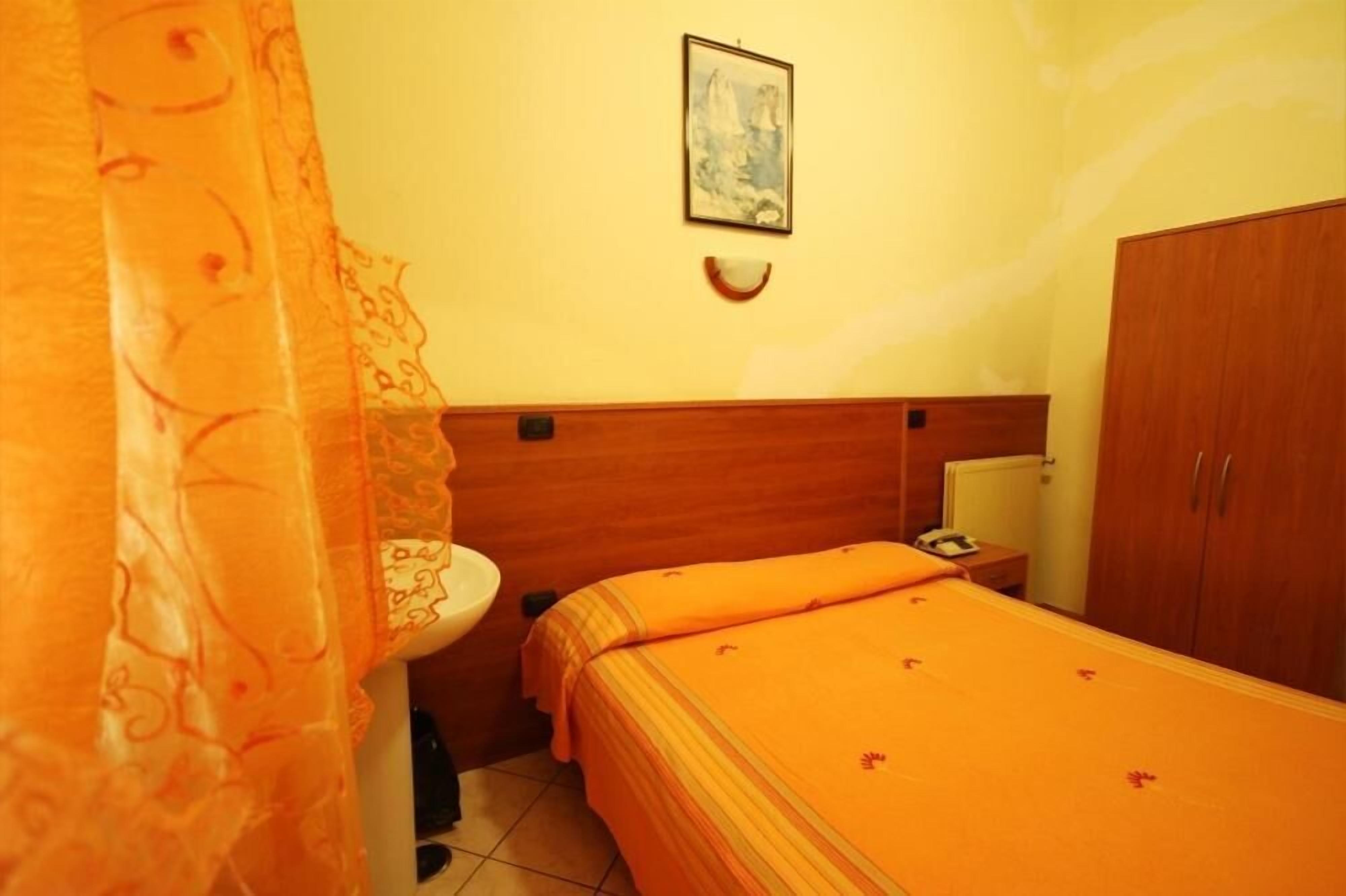 Una habitación con una cama, un armario de madera, una mesita de noche y un cuadro colgado en la pared.