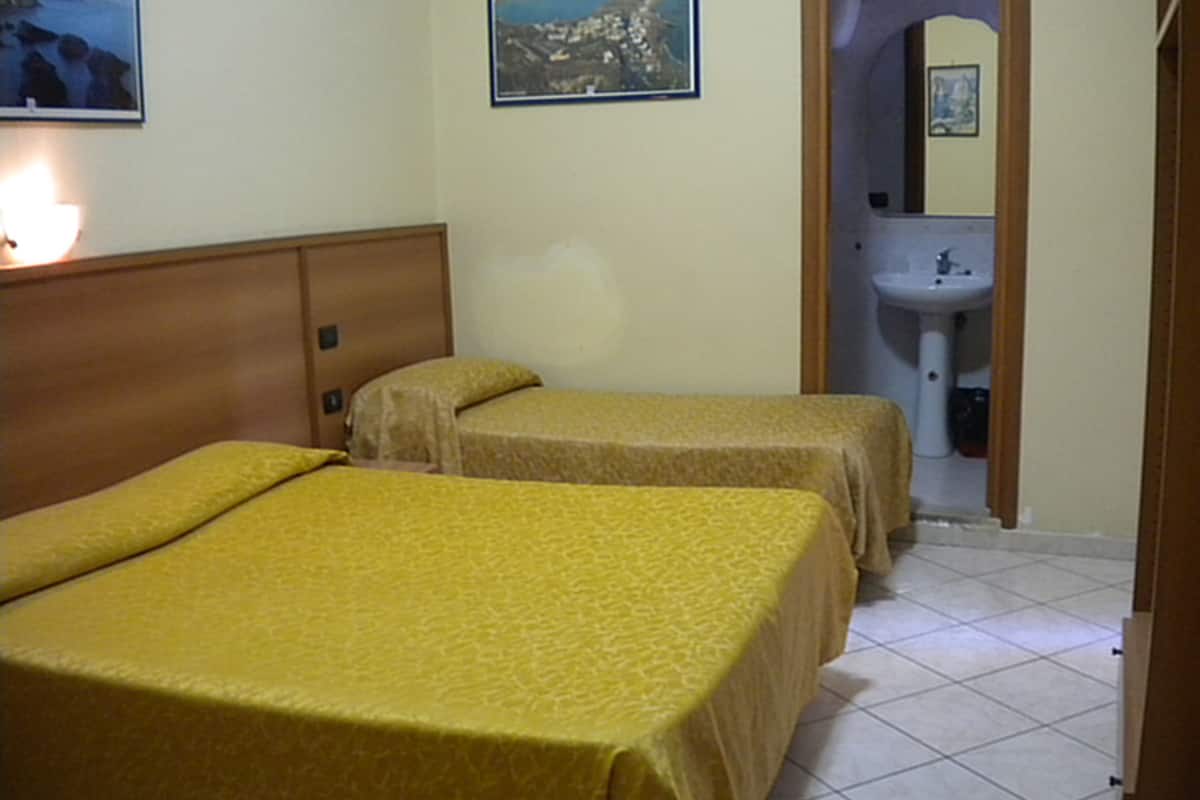 A hotel room with two beds, a wooden headboard, a framed picture on the wall, and a bathroom visible through an archway.