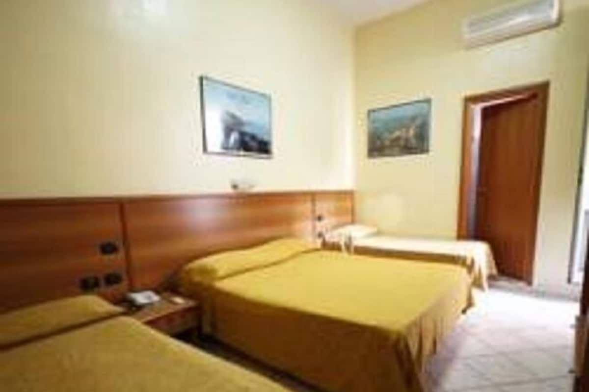 A hotel room with two beds, a wooden headboard, a nightstand, and a door.