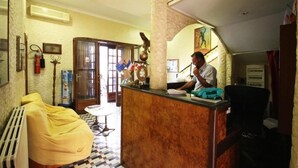 A hotel lobby with a reception desk, a yellow sofa, a radiator, and a patterned floor. - Hotel Casanova (Naples)