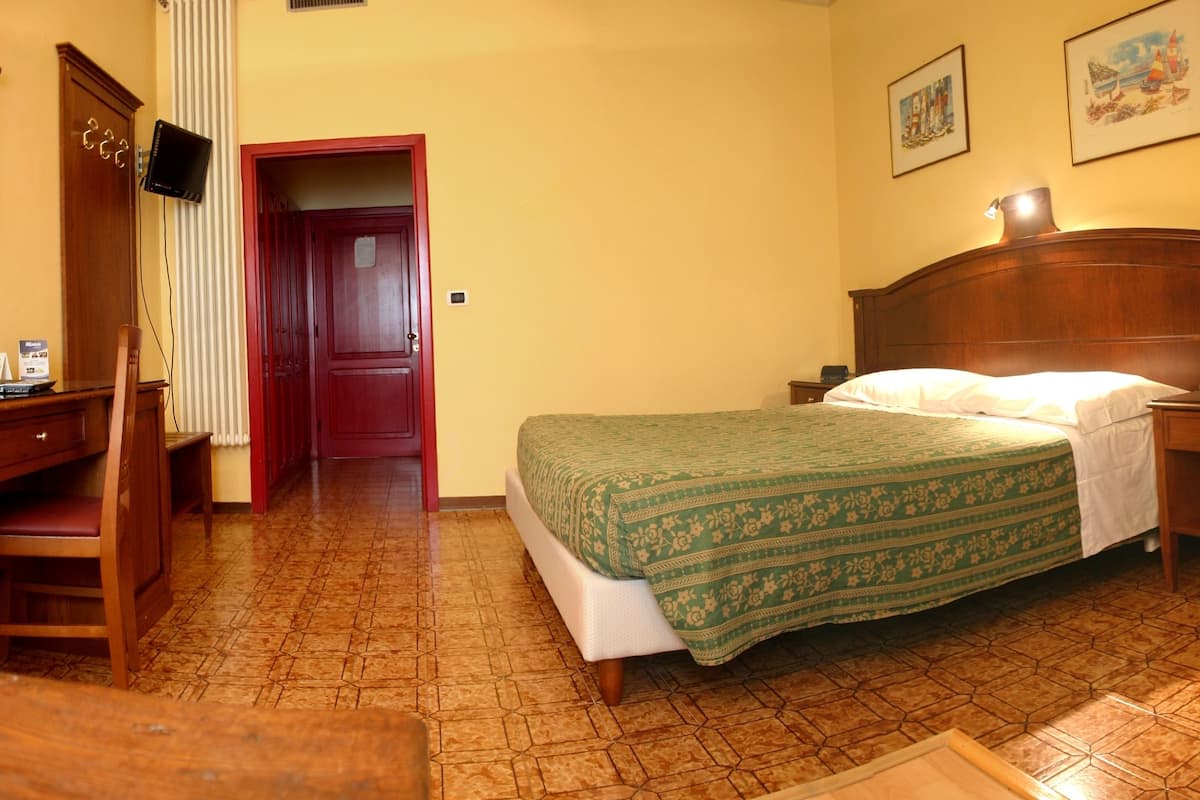 Una camera d'albergo con un letto, un comodino e una scrivania con una sedia.