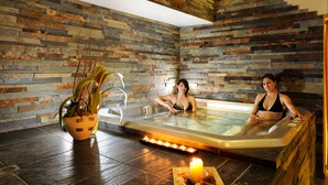 A spa area with a stone wall, a hot tub, and a candle on the floor. - Hotel Life (Rimini)