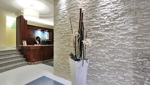 A reception area with a stone wall, a reception desk, and a staircase. - Hotel Life (Rimini)