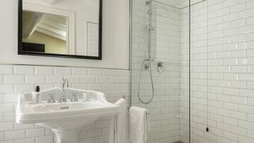 A modern bathroom with a pedestal sink, a glass-enclosed shower, and a large mirror above the sink.