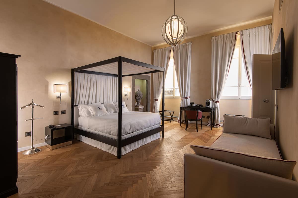 A four-poster bed with a nightstand, a desk with a chair, a sofa, and a television on the wall.