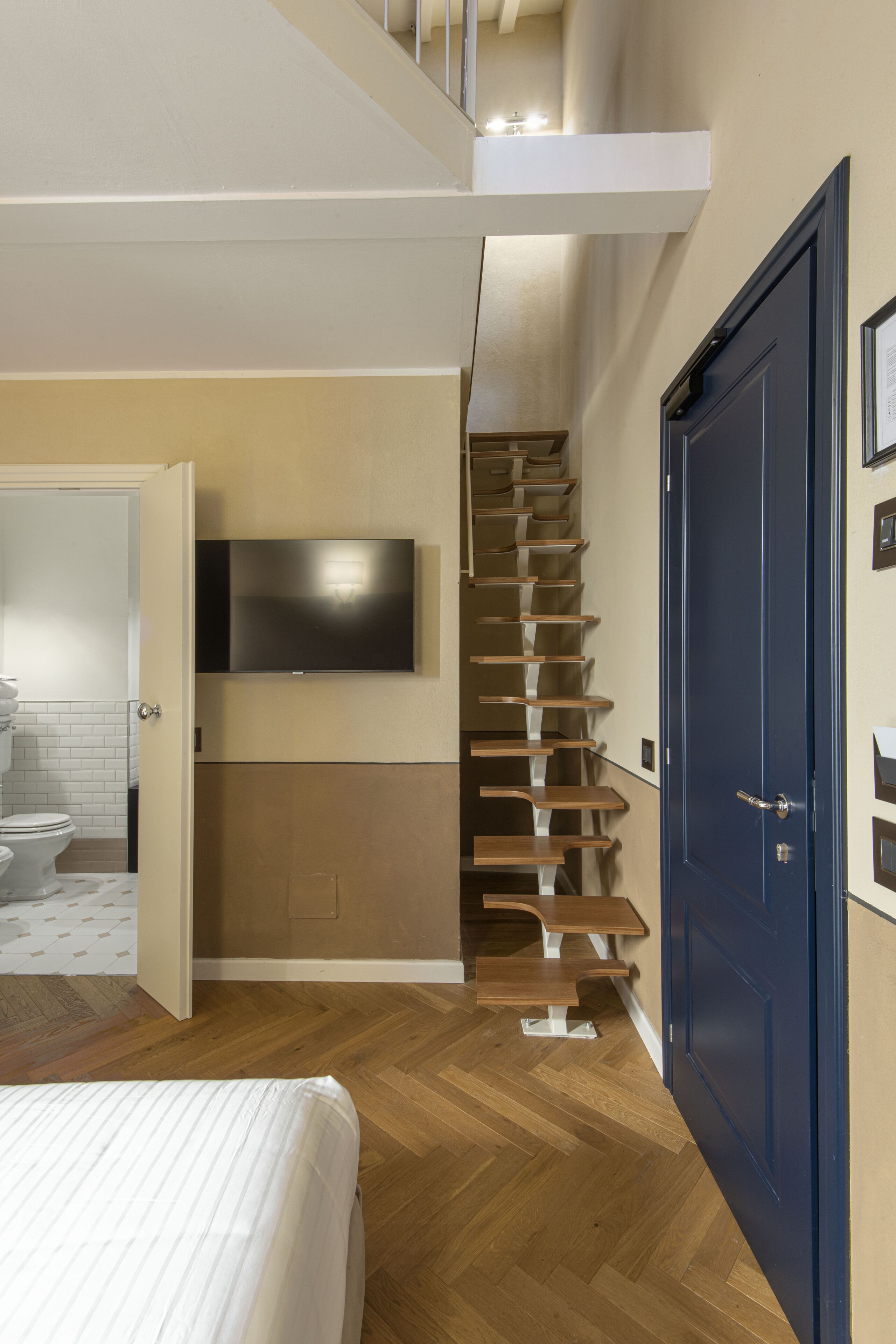 Ein Schlafzimmer mit einem Bett, einem an der Wand befestigten Fernseher, einer Holztreppe und einer blauen Tür.