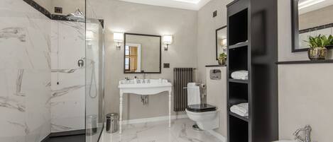 A modern bathroom with a glass shower enclosure, a white sink, a black vanity, and a bidet.