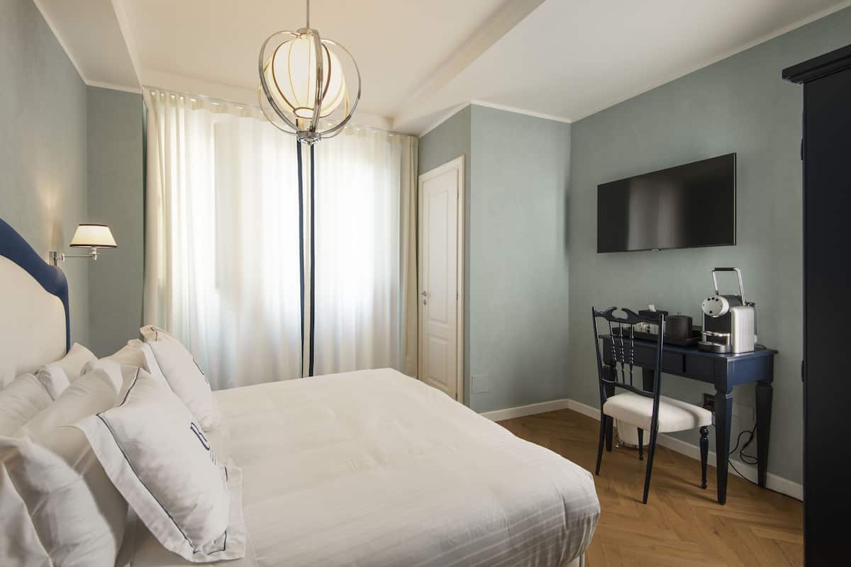 A hotel room with a large bed, a desk with a chair, a television, and a floor lamp.
