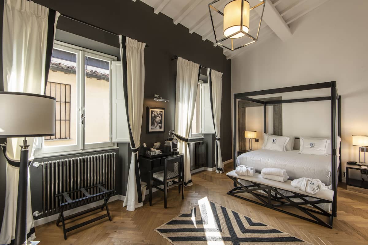 A bedroom with a four-poster bed, a desk with a chair, a radiator, and a window with curtains.
