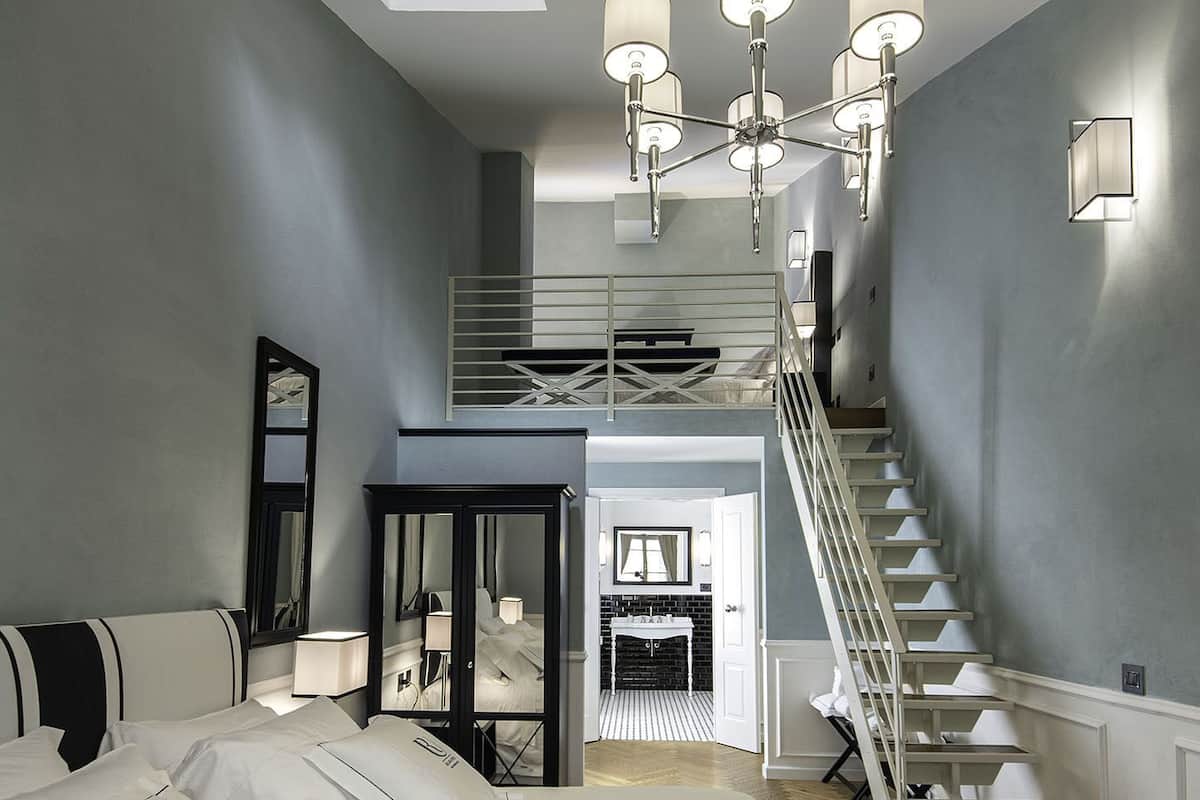 A bedroom with a bed, a desk, a chair, a mirror, a staircase, and a skylight.