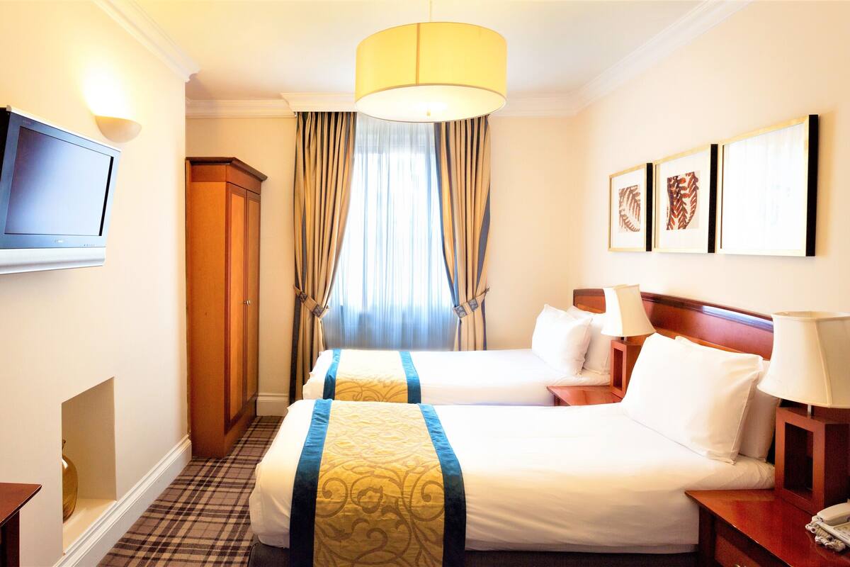 Ein Hotelzimmer mit zwei Betten, einem Fernseher, einem Schreibtisch und einem Telefon.