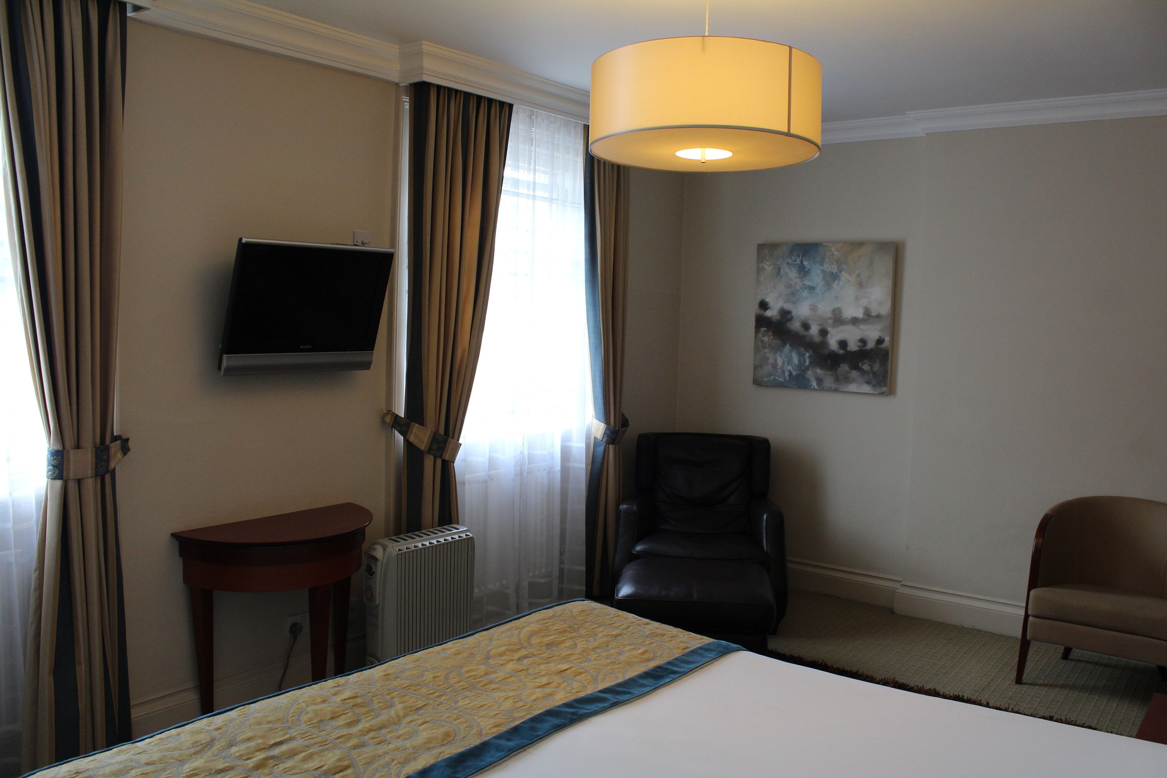 A hotel room with a bed, a chair, a television, and a painting on the wall.