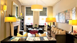 A well-lit living room with a fireplace, leather sofas, a coffee table with magazines, and a large painting on the wall. - The Sumner (London)